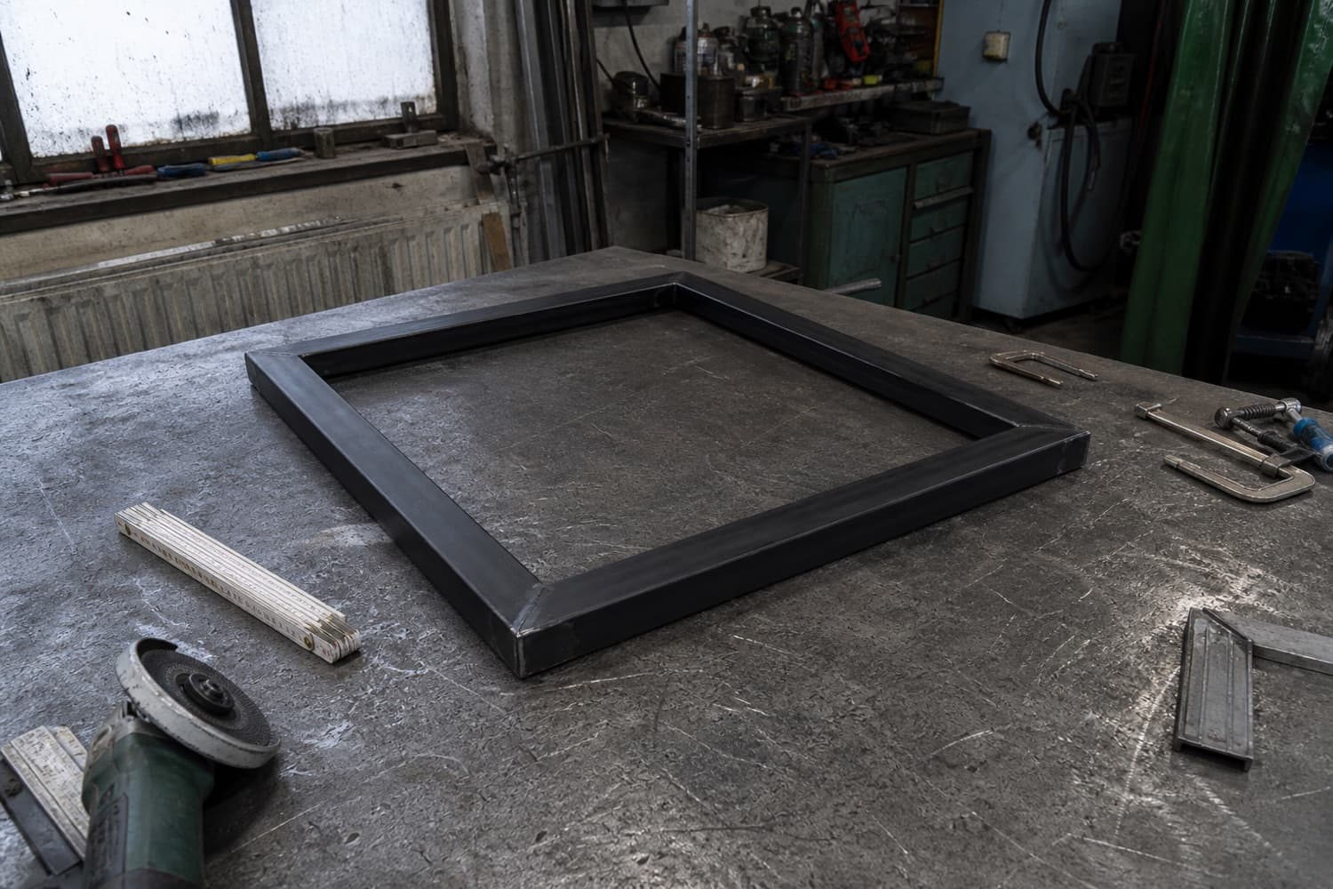 Op maat gelast stalen frame op een werkbank in een metaalwerkplaats, met bankschroeven en een haakse slijper ernaast