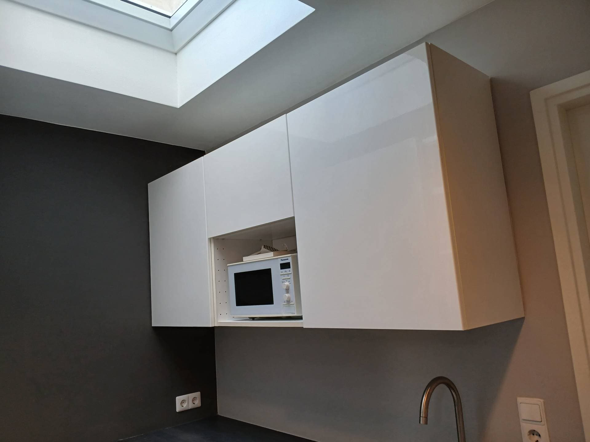 Keuken met strak afgewerkte witte hoogglans kastenwand onder een dakraam
