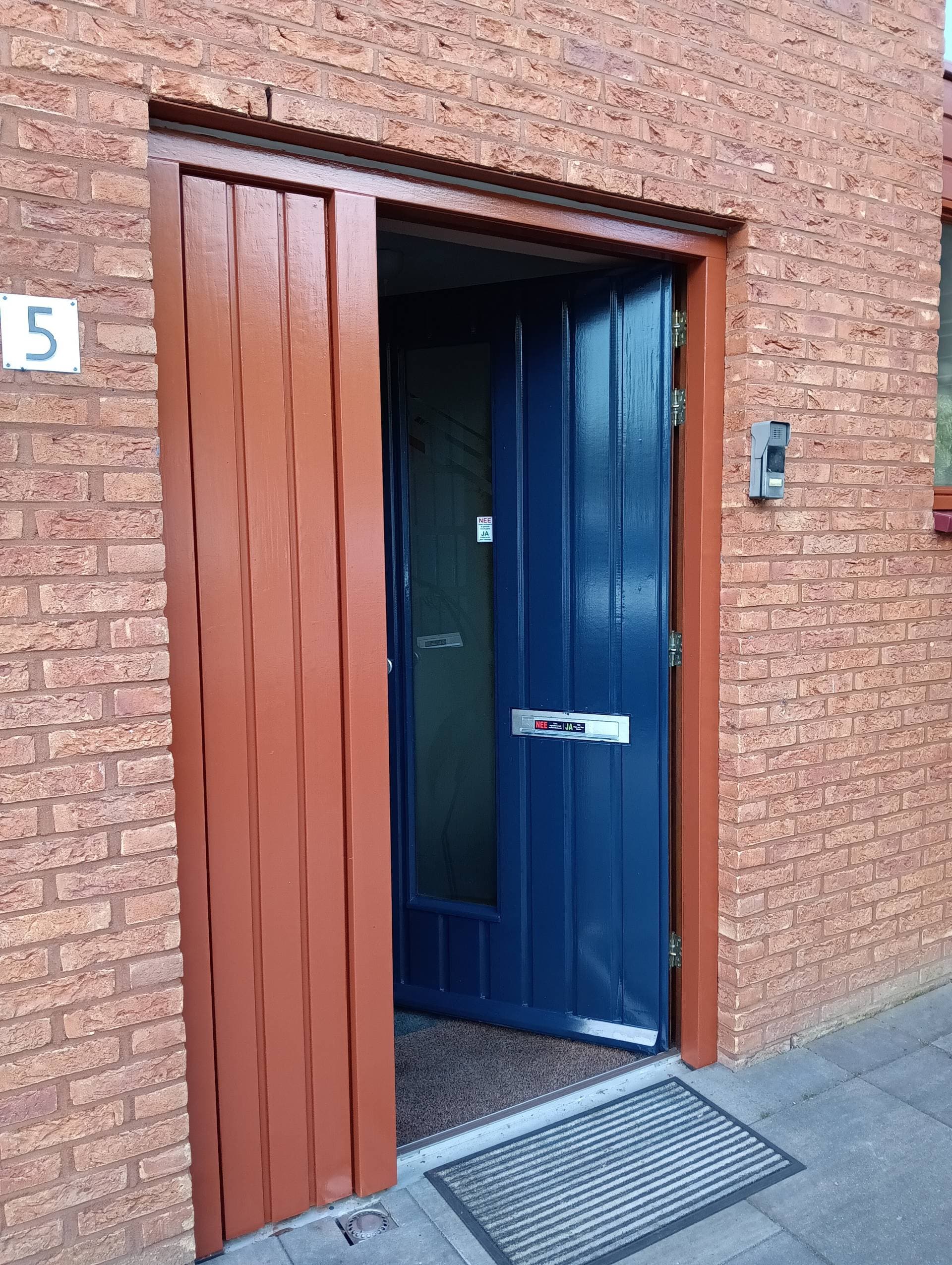 Vers gelakte voordeur en portiek, terracotta omlijsting met diepblauw deurblad